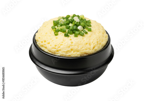 Korean Style Steamed Egg Custard Gyeran Jjim Topped with Fresh Green Onions in a Black Earthenware Bowl. Isolated on White Background.