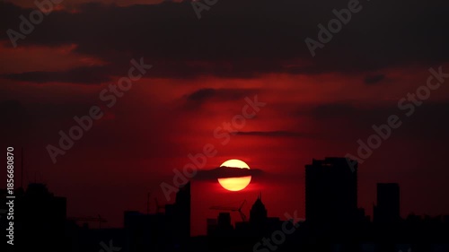 Time-lapse of the sun setting over a capital city skyline with buildings silhouetted against the sky.