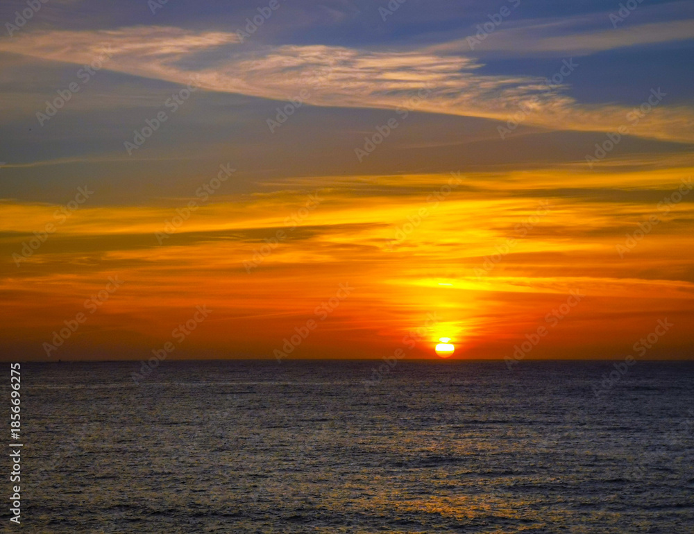 Fototapeta premium Puesta de sol anaranjada en el mar, en un entorno natural.