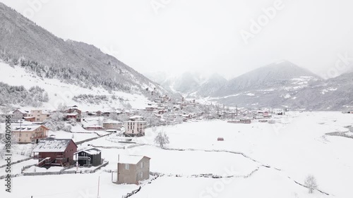 Aerial panorama mall cottages scattered on snowy slope in Caucasus mountains, surrounded by forest and alpine peaks, winter travel destination in Georgia