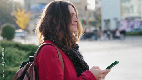 A pretty young woman uses her mobile phone while walking through the streets of a European city on a warm autumn day.