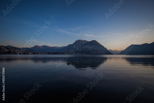 Panorama of Lugano city from the lake shore in autumn early morning with Swiss and Italian mountains in the background. Lugano, Ticino, Switzerland