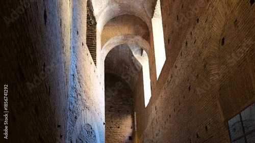 narrow ancient brick corridor high arched ceilings illuminated by sunlight streaming through irregular windows weathered hole pocked walls rome italy hole-pocked surfaces 