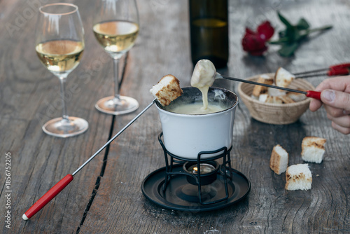Fondue with tasty melted cheese, forks, breads and wine on wooden table, closeup