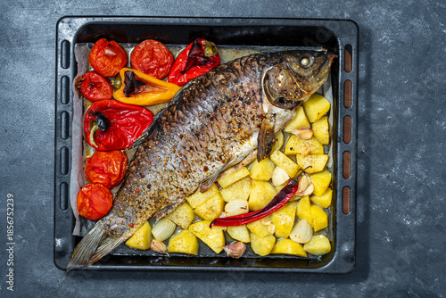 Delicious baked carp fish with spices and vegetables on a metal baking sheet, close up, top view
