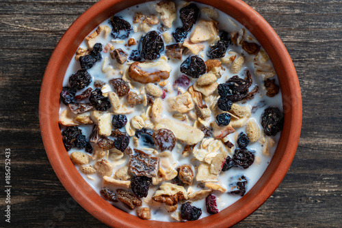 Whole grain oat muesli with dried fruits, nuts, raisins, berries and almond milk in clay bowl on wooden table, top view, closeup. Background of organic muesli for breakfast