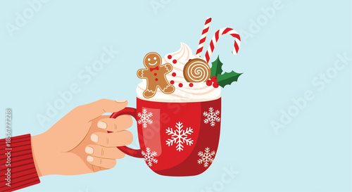 Hand holding a festive red Christmas mug of hot chocolate topped with whipped cream, a gingerbread man, and candy canes.