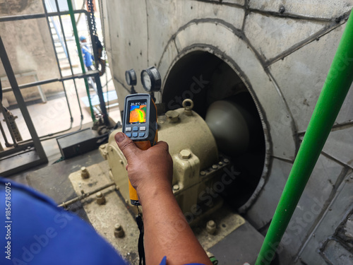 Technician using a thermal imaging camera to inspect an industrial motor and ventilation system, detecting heat patterns for preventive maintenance, safety monitoring, and equipment reliability.