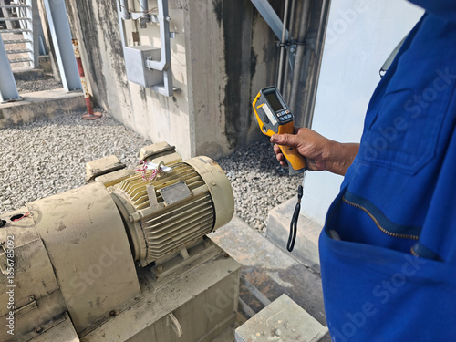 Technician using a thermal imaging camera to inspect an industrial motor and ventilation system, detecting heat patterns for preventive maintenance, safety monitoring, and equipment reliability.