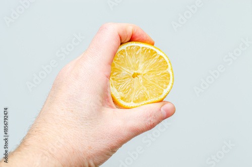 A close-up shot shows a person's hand firmly gripping a bright yellow lemon slice, highlighting its texture and freshness