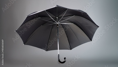 a black umbrella with a curved handle stands open against a plain gray background open umbrella
