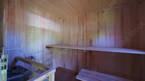 cozy sauna room with light wooden walls and ceiling, built-in wooden bench, upper shelf, tiled stove corner, small window for ventilation