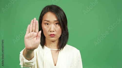 Woman on green screen demonstrates stop gesture for safety.
