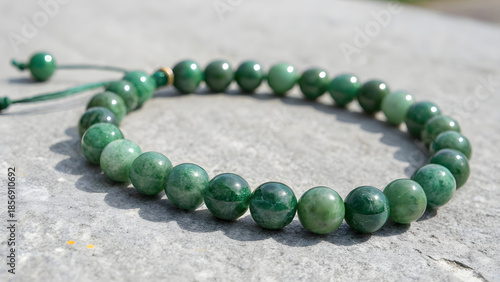 A delicate green beaded bracelet rests in a gentle arc on a smooth, matte gray concrete surface, its beads—polished jade, malachite, or artisan glass—gleaming with a soft