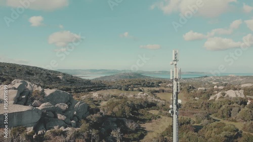 Aerial drone footage flying over a rural countryside valley characterized by rocky terrain and scattered shrubs. In  the landscape stands a telecommunications tower used for mobile and wireless 
