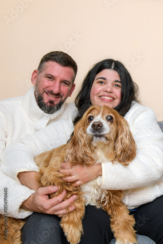 Smiling couple holding their dog while sitting together indoors.
