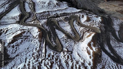 Winding mountain road switchbacks through snowy hills aerial view