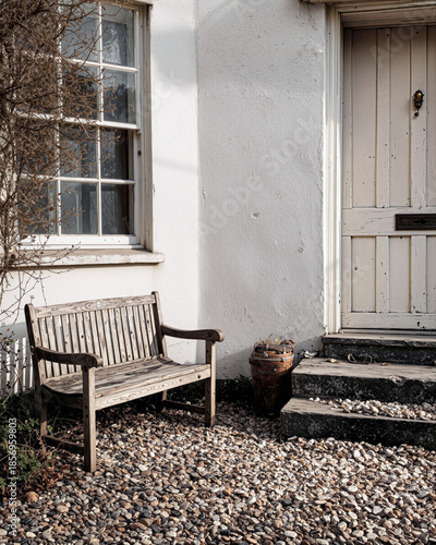 Rustic wooden bench outside white cottage entrance with vintage door and climbing vines