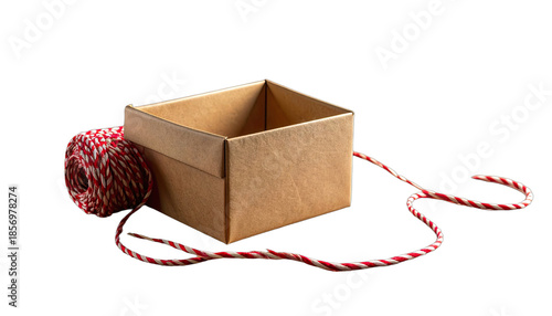 An empty brown cardboard box sits next to a spool of red and white baker's twine against a stark black background.