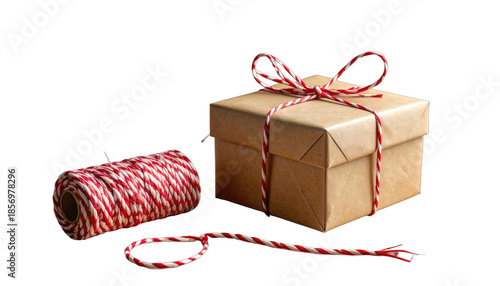 A simple brown gift box wrapped with red and white baker's twine sits beside its spool against a black background.