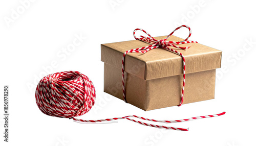 A simple brown gift box tied with red and white baker's twine next to a ball of matching twine on a black background.