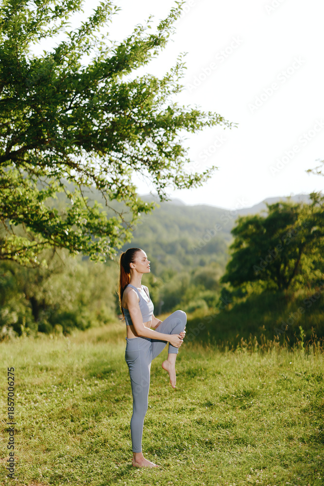Fototapeta premium Young woman practicing yoga outdoors, showcasing flexibility and balance in a serene green setting, reflecting calmness and health
