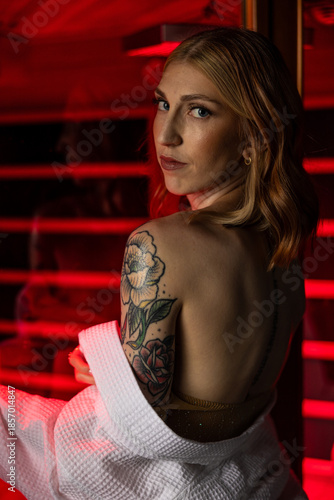 Fotografía Artistic sauna portrait of an adult woman glancing over her shoulder inside a red-lit steam room