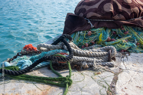 Fishermans equipment lying on the coastline in harbor, heap nylon yellow tangled fishing net in sunlight, colorful ropes