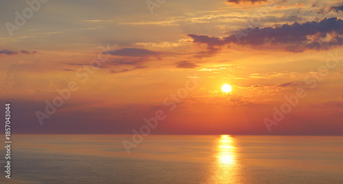 Golden sunset over calm sea with dramatic clouds and colorful sky reflected on water, concept of peace, serenity, inspiration and natural beauty in horizontal landscape