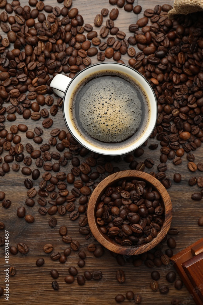 Fototapeta premium Aromatic coffee in cup and beans on wooden table, flat lay
