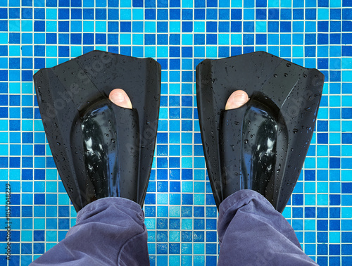 Wet black swimming flippers on feet standing on tiled surface of swimming pool. Close-up of diving equipment after water activity