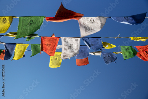 Fotografi Tibetan prayer flags hang in the clear sky above a Buddhist temple, showing vibr
