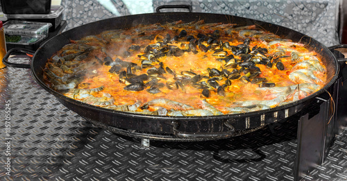Photos giant paella pan brimming with rice, mussels, shrimp, and vegetables simmers ove