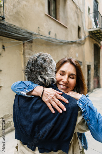 Happy senior adult woman embracing her husband with eyes closed, showing affection and strong bond while enjoying a loving moment together on a narrow street in barcelona