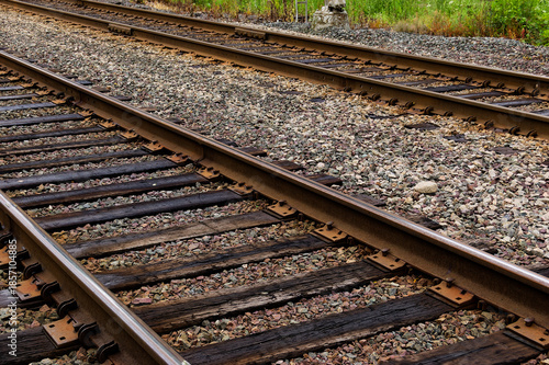Transportation Infrastructure: Close-Up of Railway Tracks with Wooden Sleepers and Gravel Ballast Lined by Greenery in Rural Setting