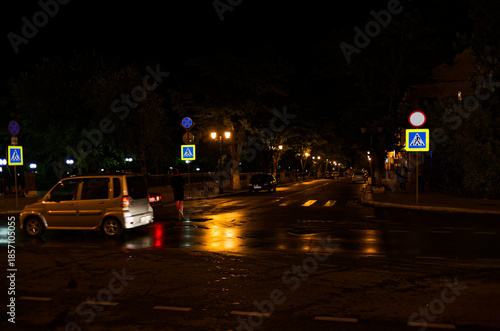 Wallpaper Mural Urban Night Scene: Vehicles Navigating Quiet City Intersection under Streetlights and Reflective Wet Road Surface, Horizontal Shot Torontodigital.ca