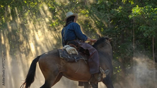 A cowboy riding a horse through dramatic rays of sunlight shining between the trees, creating a cinematic western atmosphere