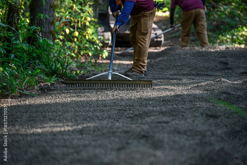 Obraz premium Landscaping maintenance crew using rakes and spreading freshly laid gravel on a woodland trail in a forest park 
