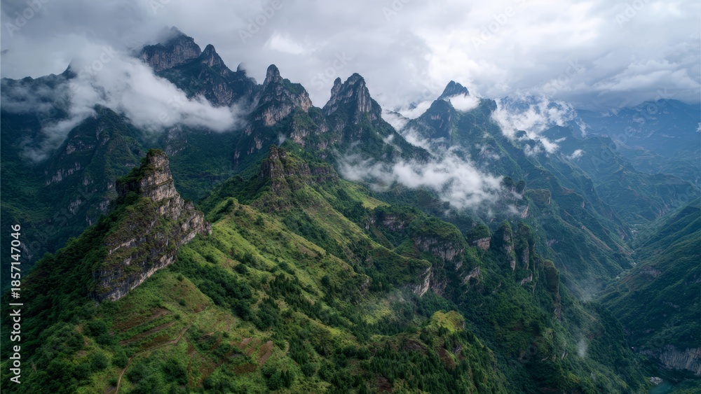 Fototapeta premium Jagged green mountain peaks emerge from atmospheric clouds in a misty rugged landscape