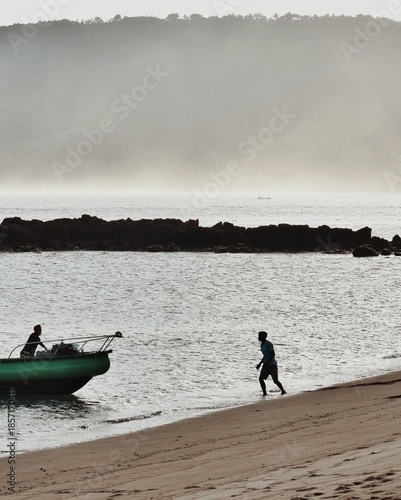 A person is walking on the beach, heading for a boat in Lombok