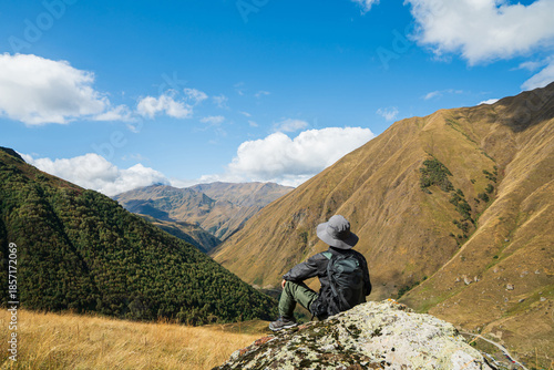 Wallpaper Mural A solo hiker sitting on a mountain rock and admiring scenic nature views in Juta Village, Georgia. Adventure travel lifestyle, freedom in the Caucasus mountains under a bright blue sky. Torontodigital.ca