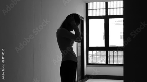 A lonely young woman sits on the floor in a narrow hallway, clutching her head in despair, expressing sadness, stress, and emotional conflict in the quiet, simple interior of the building. The image i
