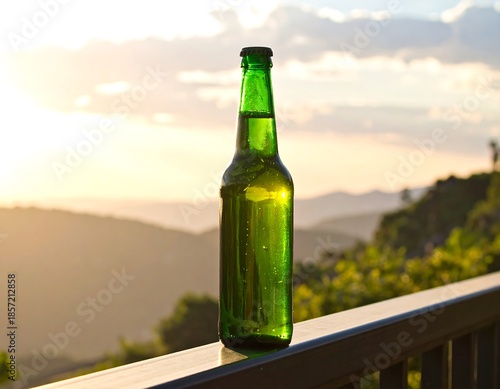 Green glass bottle stands on a railing with a sunset over mountainous landscape