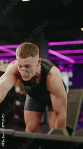 A determined male athlete performs dumbbell rows in a modern gym. He focuses on building back strength and muscle. This fitness video showcases dedication and a healthy lifestyle in a vibrant,