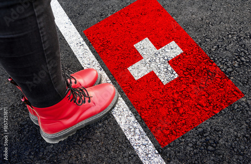 a woman with a boots standing on asphalt next to flag of Switzerland and border
