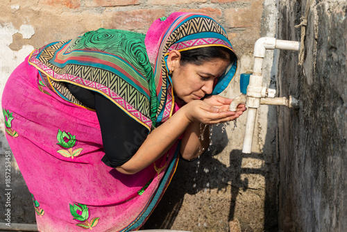 Photography Thirsty rural Indian woman drinking fresh clean water from a tap outdoor, People of India