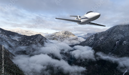 Private Jet Soaring Over Snowy Mountain Range Above Cloudy Valley in British Columbia