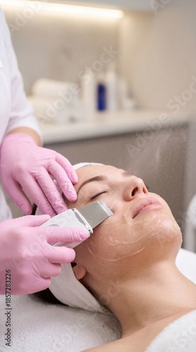 Ultrasonic skin scrubber facial treatment with pink gloves close up
