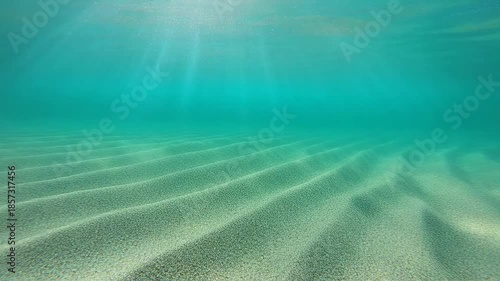 Underwater scene with sunlight rays illuminating sandy ocean floor.