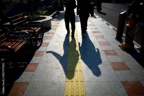Yellow tactile paving for blind people or visually impaired and human shadow on the sidewalk